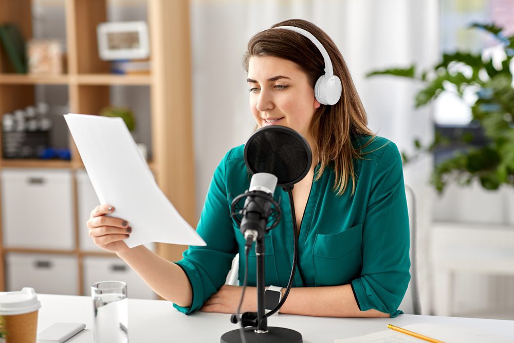 Woman reading script in front of a microphone.