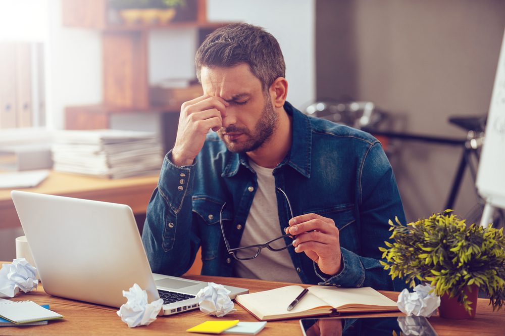 Man stressed at work with crumbled papers on desk.