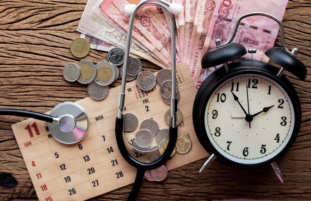 Money, clock, calendar and stethoscope on wooden table. 
