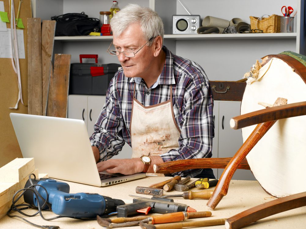Old man using laptop in a workshop.
