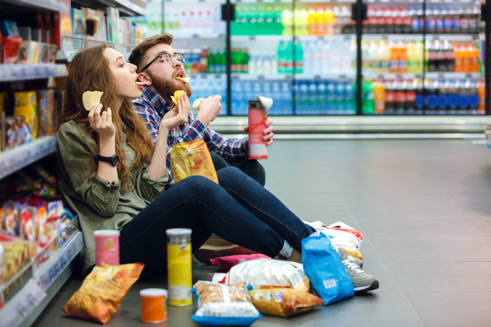 Couple sitting in a grocery stole isle, eating junkfood.