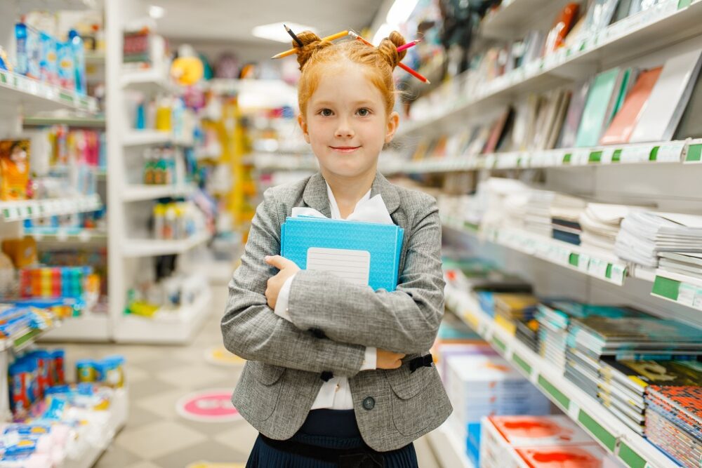 Little school girl with notebooks in stationery store. Female child buying office supplies in shop, schoolchild in supermarket